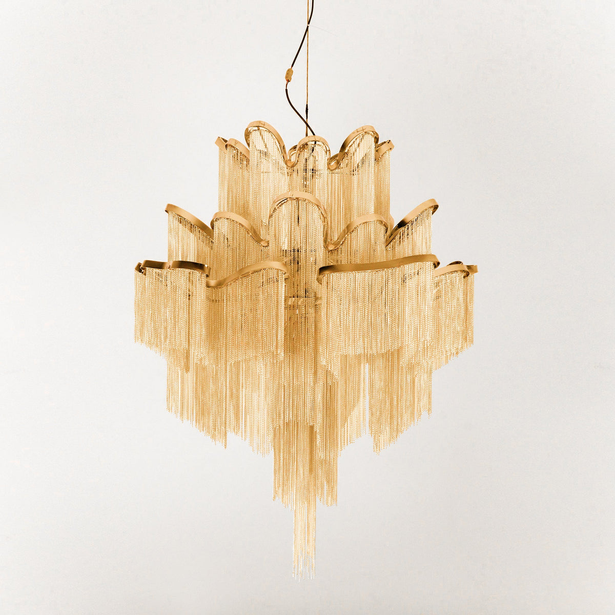 This gold Clérachic chandelier is shown unlit against a cream backdrop, its tiers fully spread.