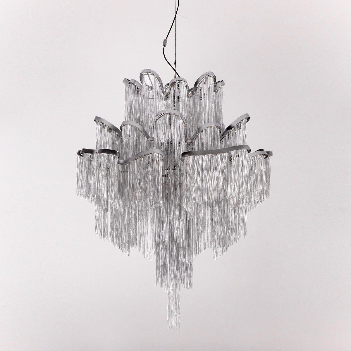 A silver Clérachic chandelier is shown unlit against a light grey backdrop, its chain tiers catching the light.