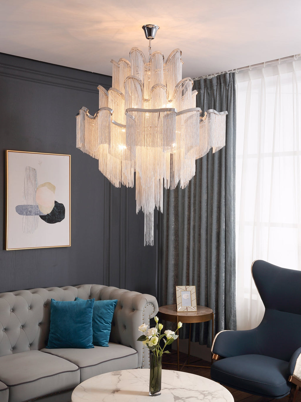 Above a marble coffee table and framed art, this lit silver Clérachic chandelier hangs beside teal sofa cushions.