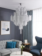 Cropped closer against sheer curtains, this lit silver Clérachic chandelier is shown in a grey-toned living room.