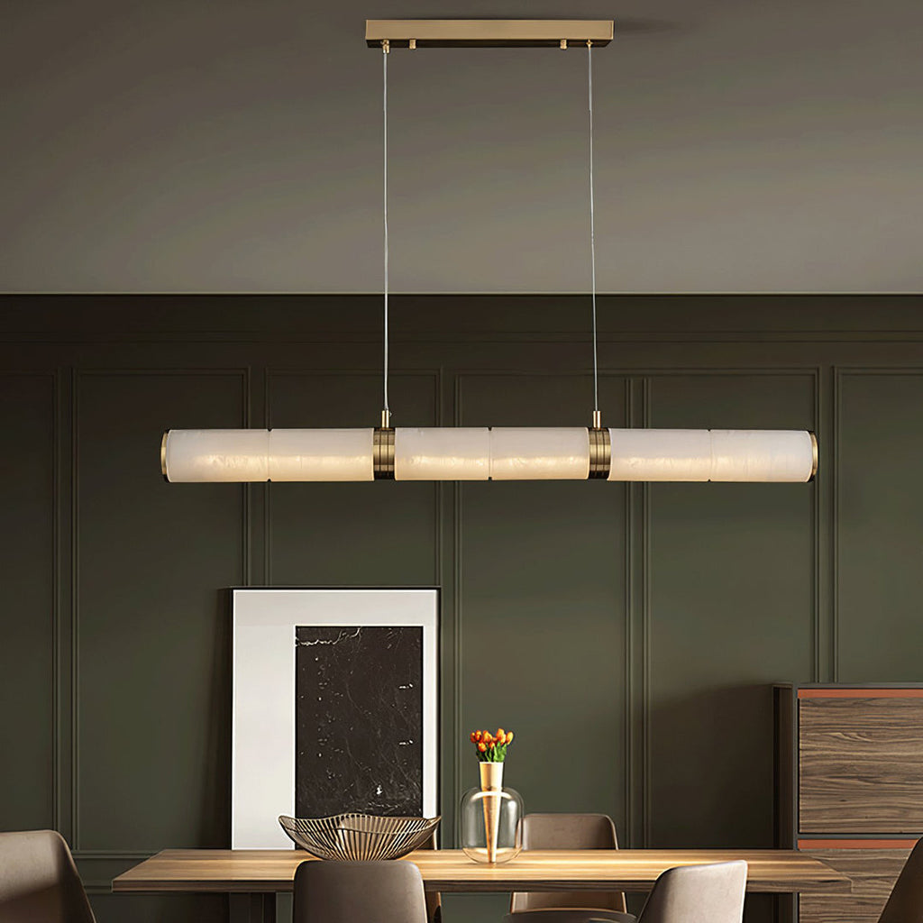 The pendant lit in a green panelled dining room, above a timber table set with orange tulips.