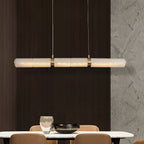 The Stream pendant lit above a dining table, set against dark timber panelling and a veined marble wall.