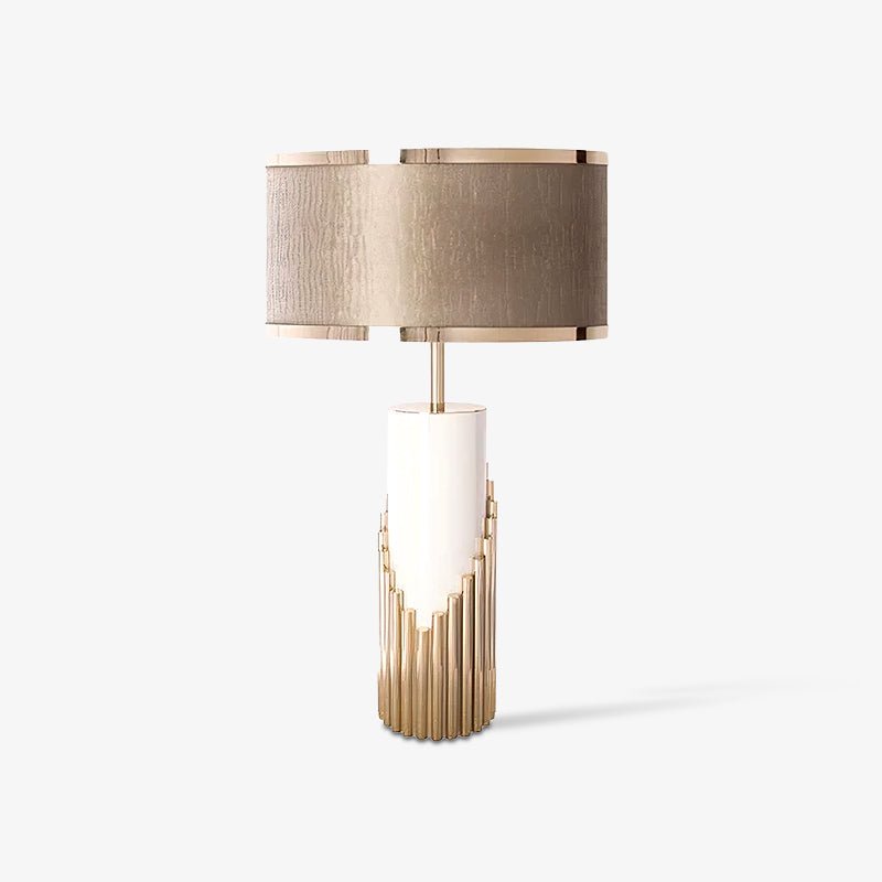 This Clérachic table lamp stands alone on a plain grey backdrop, its champagne drum shade sitting atop a stepped gold-tube base.