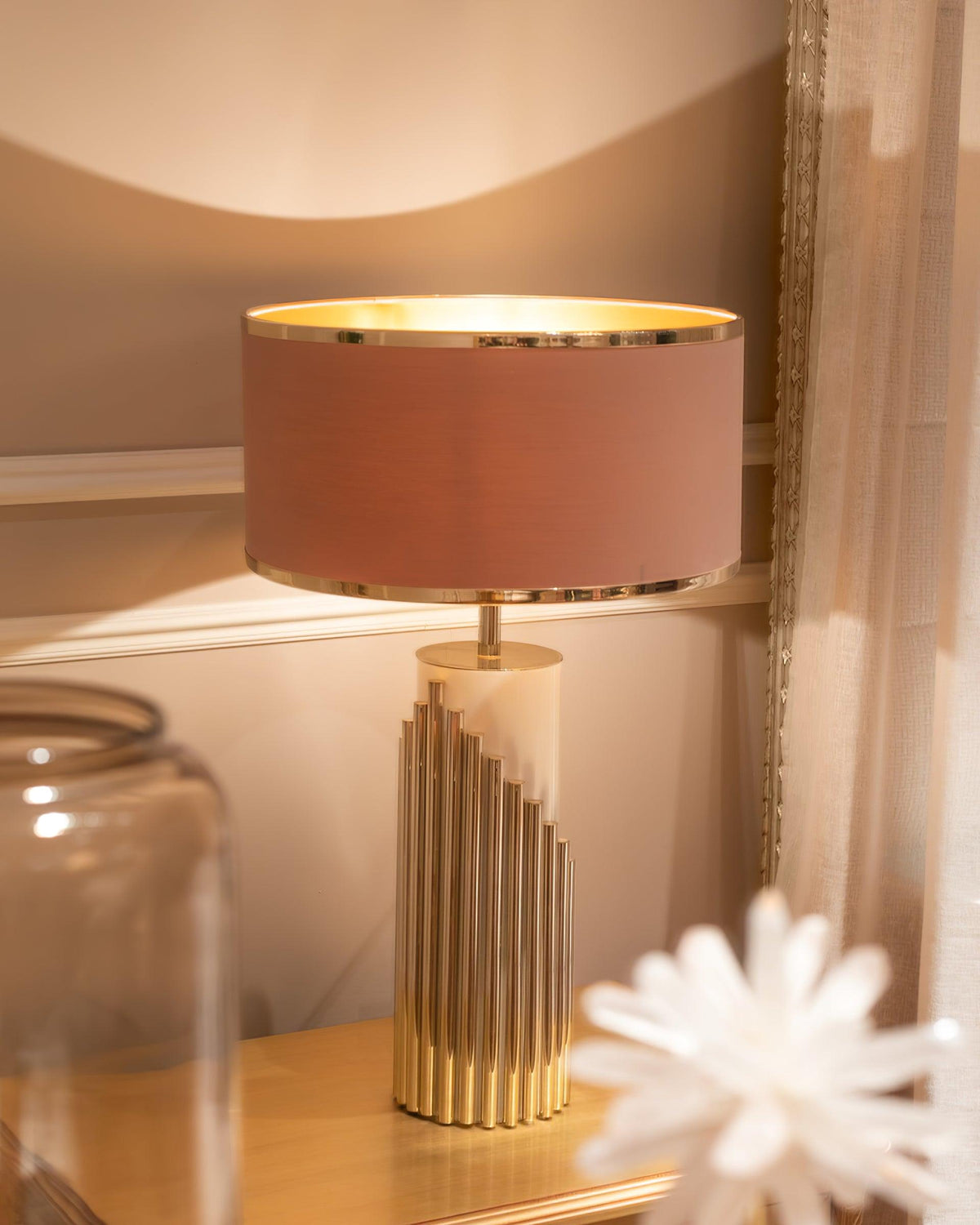 Close up, a rust-toned drum shade glows warm on this Clérachic lamp, set on a nightstand beside a glass jar and a crystal ornament.