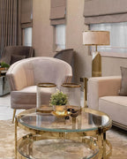 In a living room with blush armchairs and a glass coffee table, this Clérachic table lamp glows softly in the background.