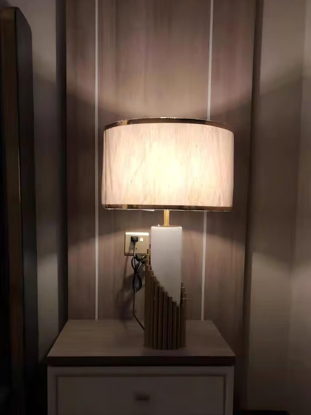 Switched on and glowing warm, this Clérachic table lamp sits on a striped-wallpaper nightstand with its cord visible.