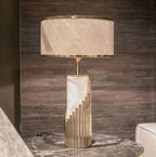 In a dark-panelled bedroom, this Clérachic lamp's white marble column rises from a stepped brass base beside a veined stone table.