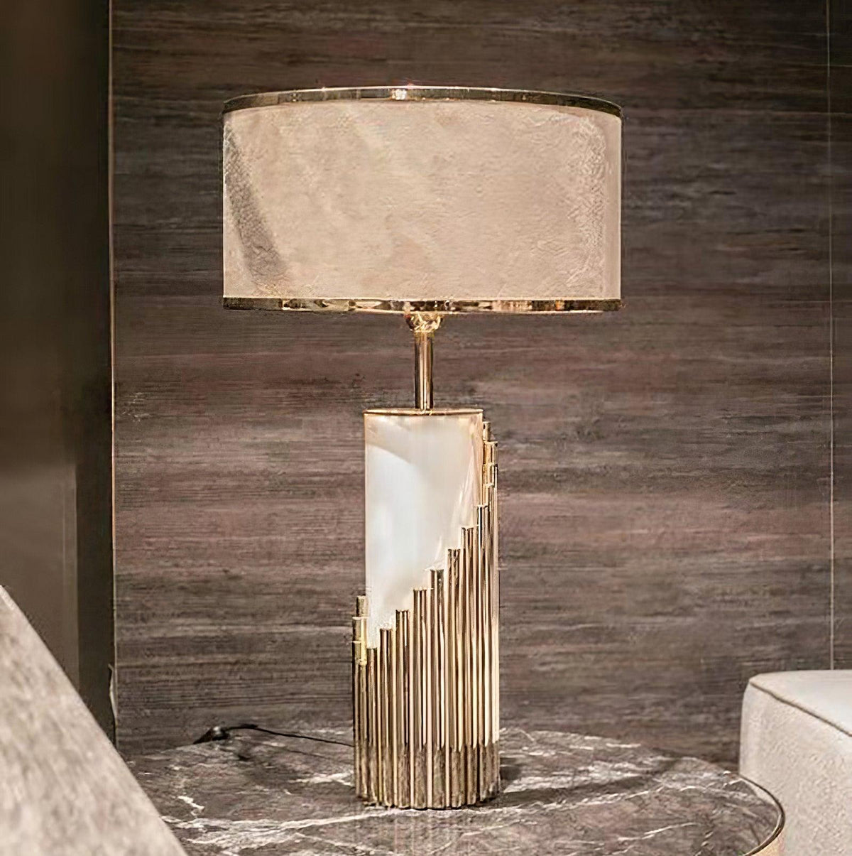 In a dark-panelled bedroom, this Clérachic lamp's white marble column rises from a stepped brass base beside a veined stone table.