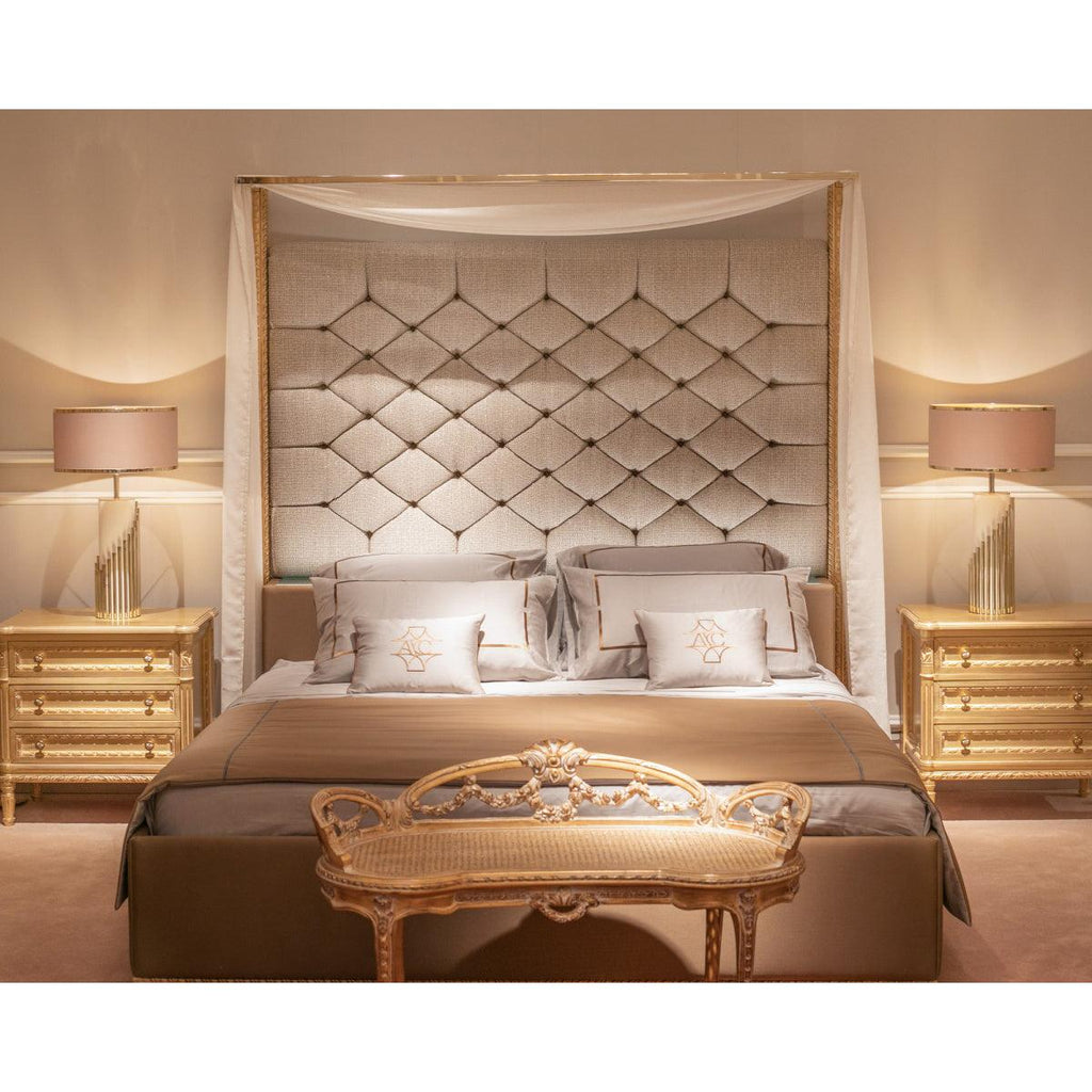 In this Clérachic bedroom scene, two stepped-base table lamps with pale pink shades flank a canopy bed on gold nightstands.