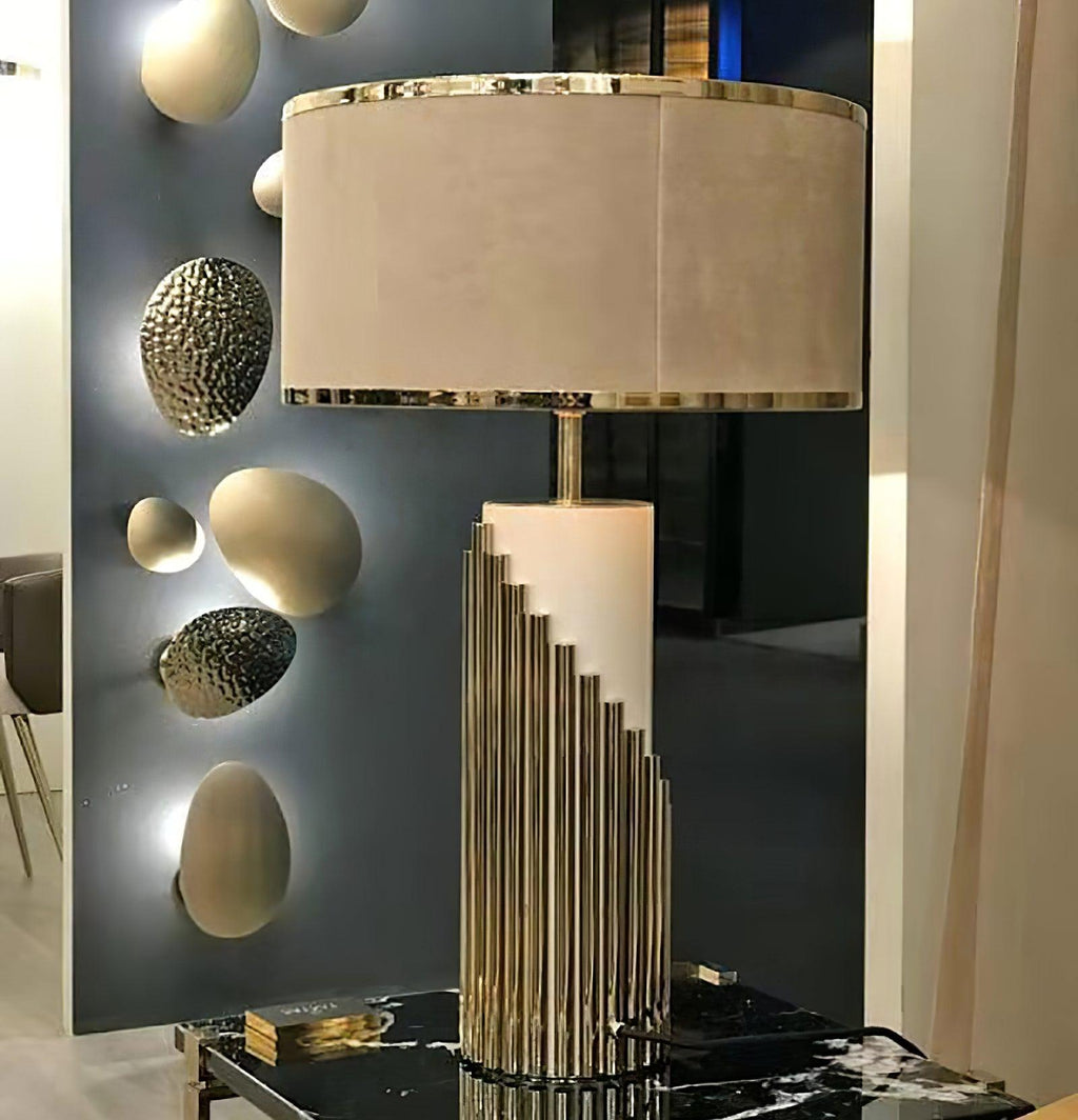 A close-up shows this Clérachic lamp's stepped gold-tube base on a black table, set against a dark mirror with sculpted spheres.