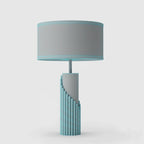 Shown here in a teal-blue colourway, this Clérachic table lamp's stepped ribbed base sits against a plain grey backdrop.