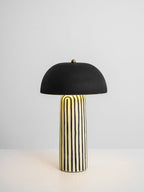Set on a plain light surface, this Clérachic table lamp shows its striped ceramic base beneath the matte black dome.