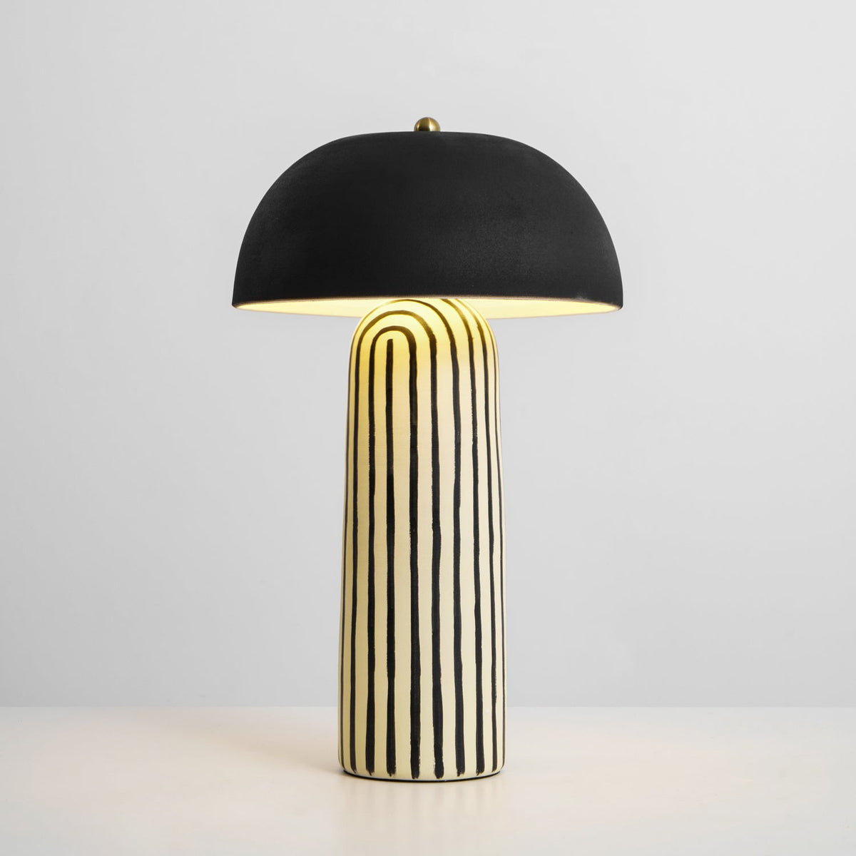 Lit against a plain light background, this Clérachic table lamp's dome glows warmly above the black-and-white striped base.