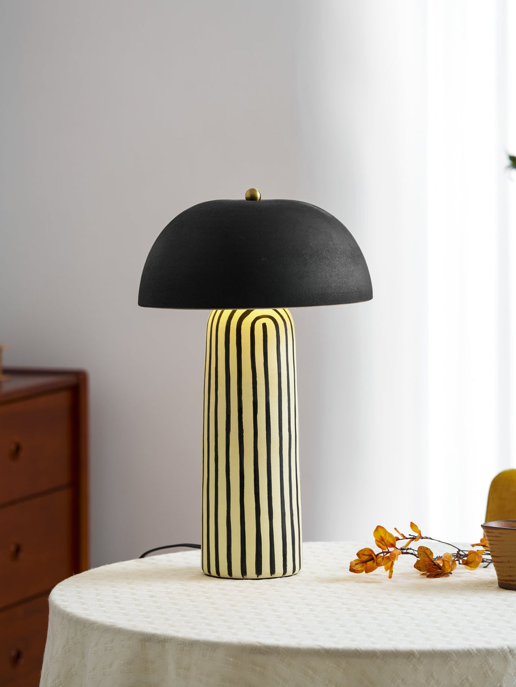 Beside a spray of dried orange berries, this Clérachic table lamp stands on a round linen-covered table.
