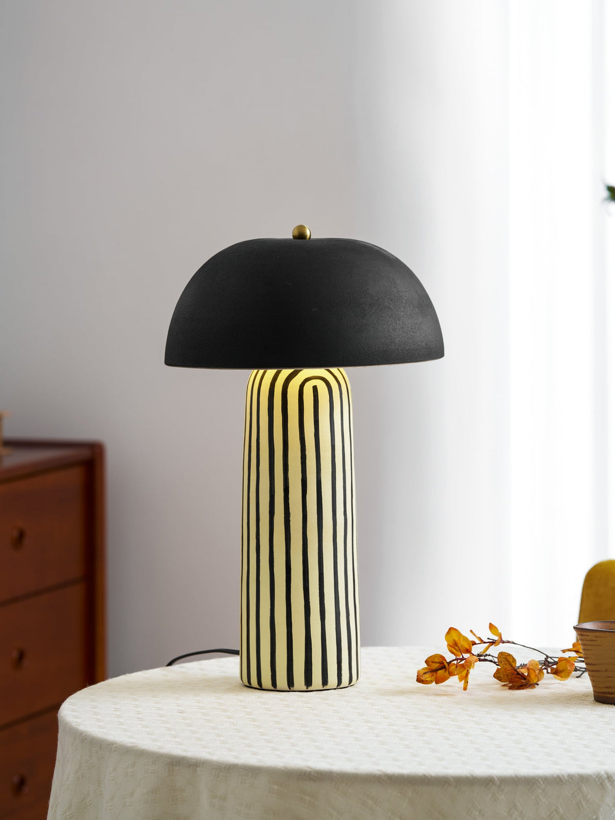 Beside a spray of dried orange berries, this Clérachic table lamp stands on a round linen-covered table.