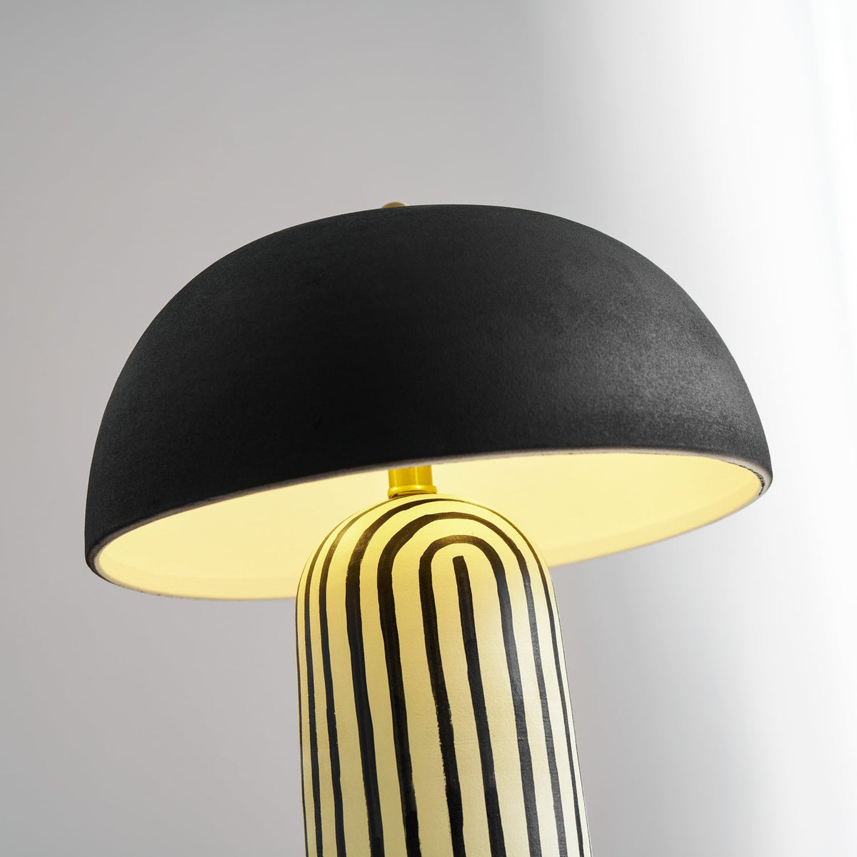 A low upward angle looks into the shade of this Clérachic table lamp, its striped ceramic base rising below the black dome.