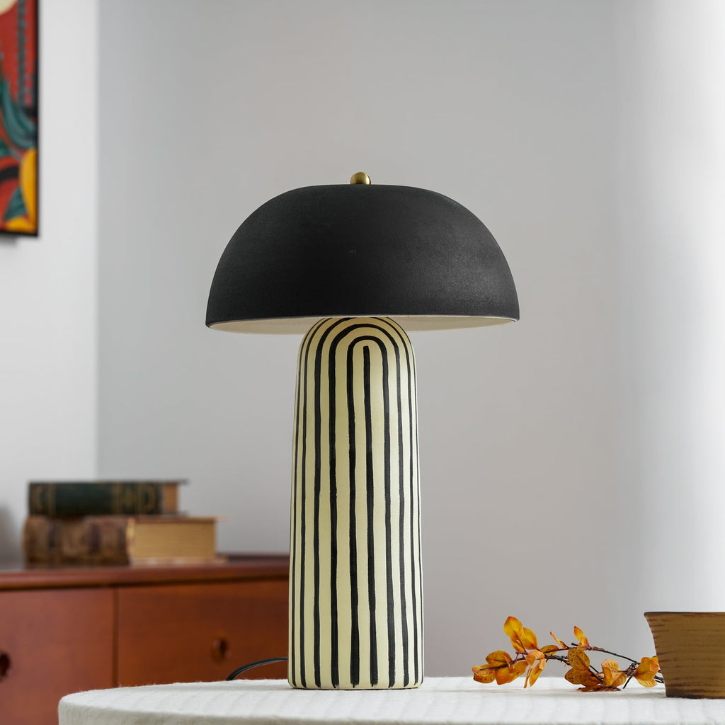 Books and a framed abstract painting sit behind this Clérachic table lamp, styled on a round table beside a wood dresser.