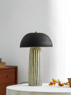 Against a plain white wall, this Clérachic table lamp stands on a round linen-covered table beside a berry branch.