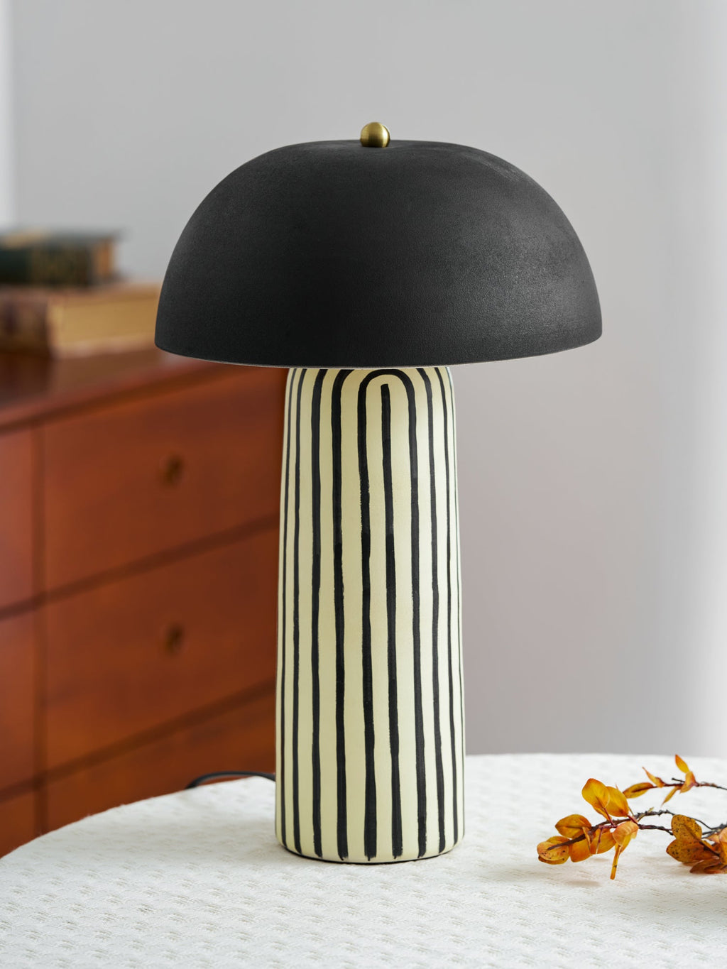 A stack of books sits behind this Clérachic table lamp on a round table, a wood dresser in the background.