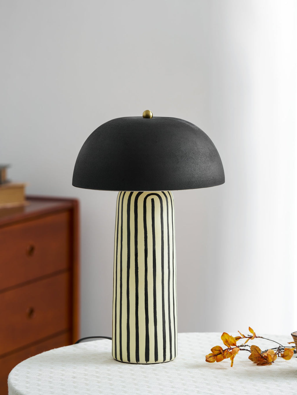 A spray of dried berries sits beside this Clérachic table lamp on a round linen-covered table.