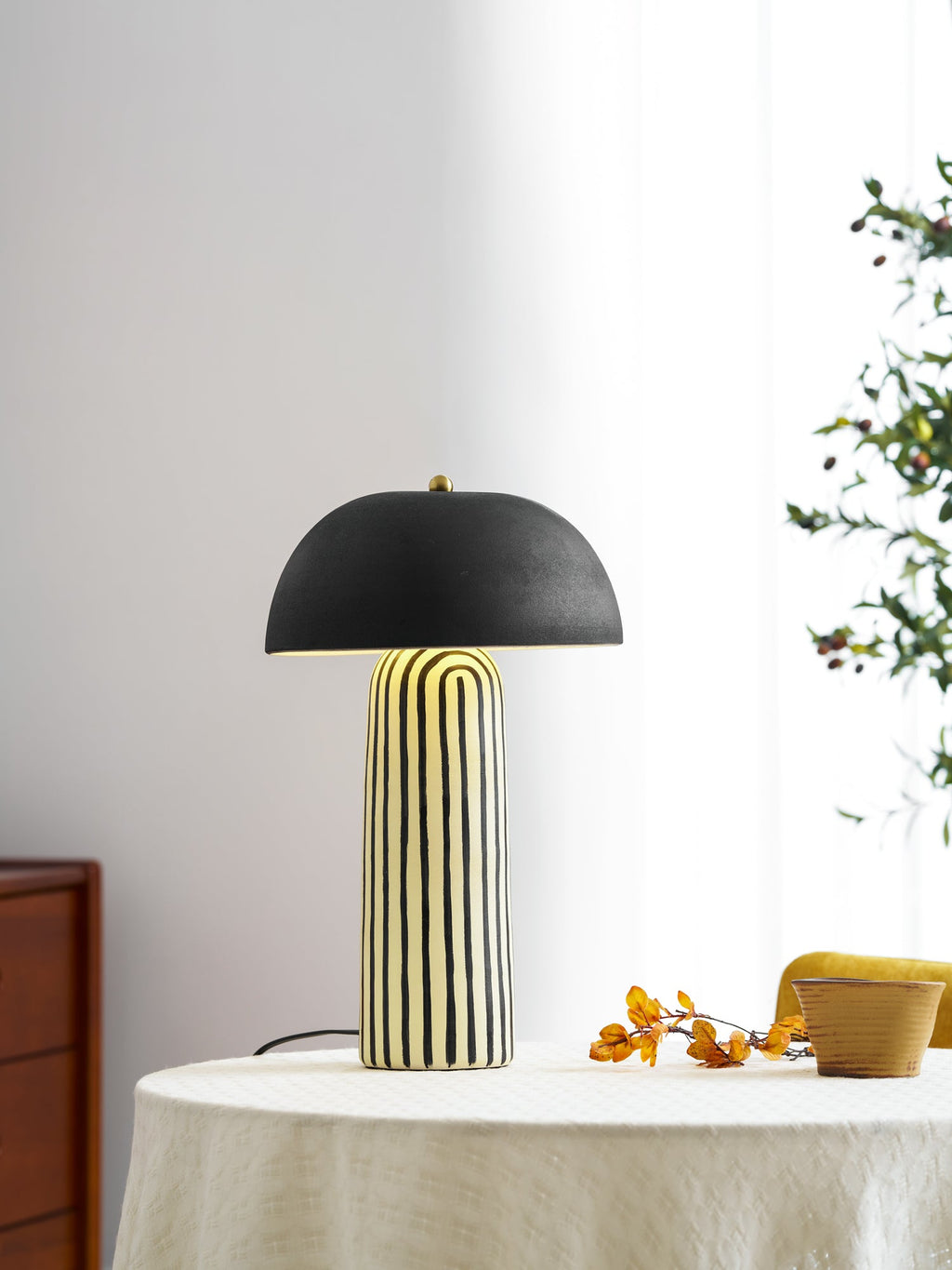 A sheer curtain and green branch frame this Clérachic table lamp, styled on a round table.