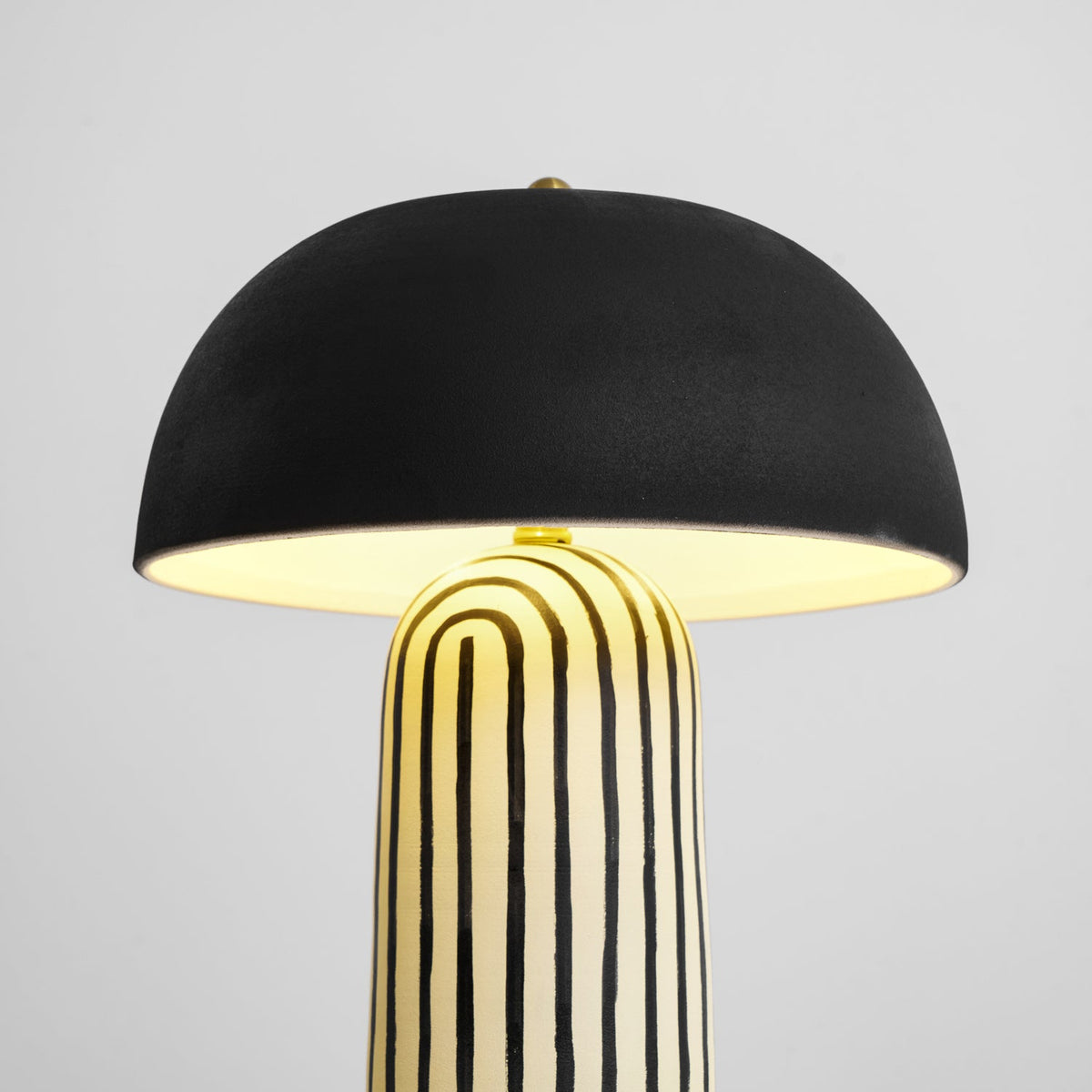 Lit on a plain backdrop, this Clérachic table lamp's dome shade glows warmly above the black-and-white striped base.