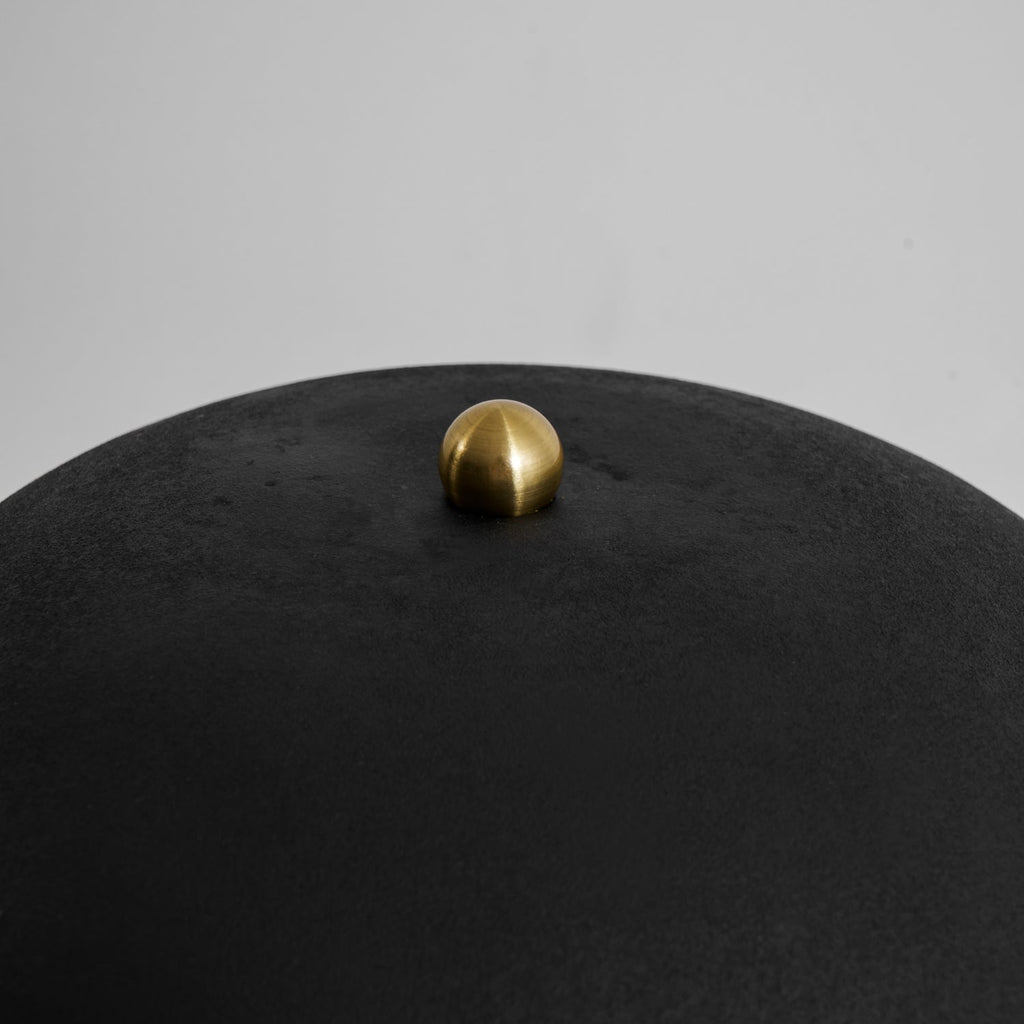 A close-up shows the brass finial atop this Clérachic table lamp's matte black dome shade.