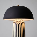 A close studio view of this Clérachic table lamp shows its matte black dome shade above the hand-painted striped ceramic base.