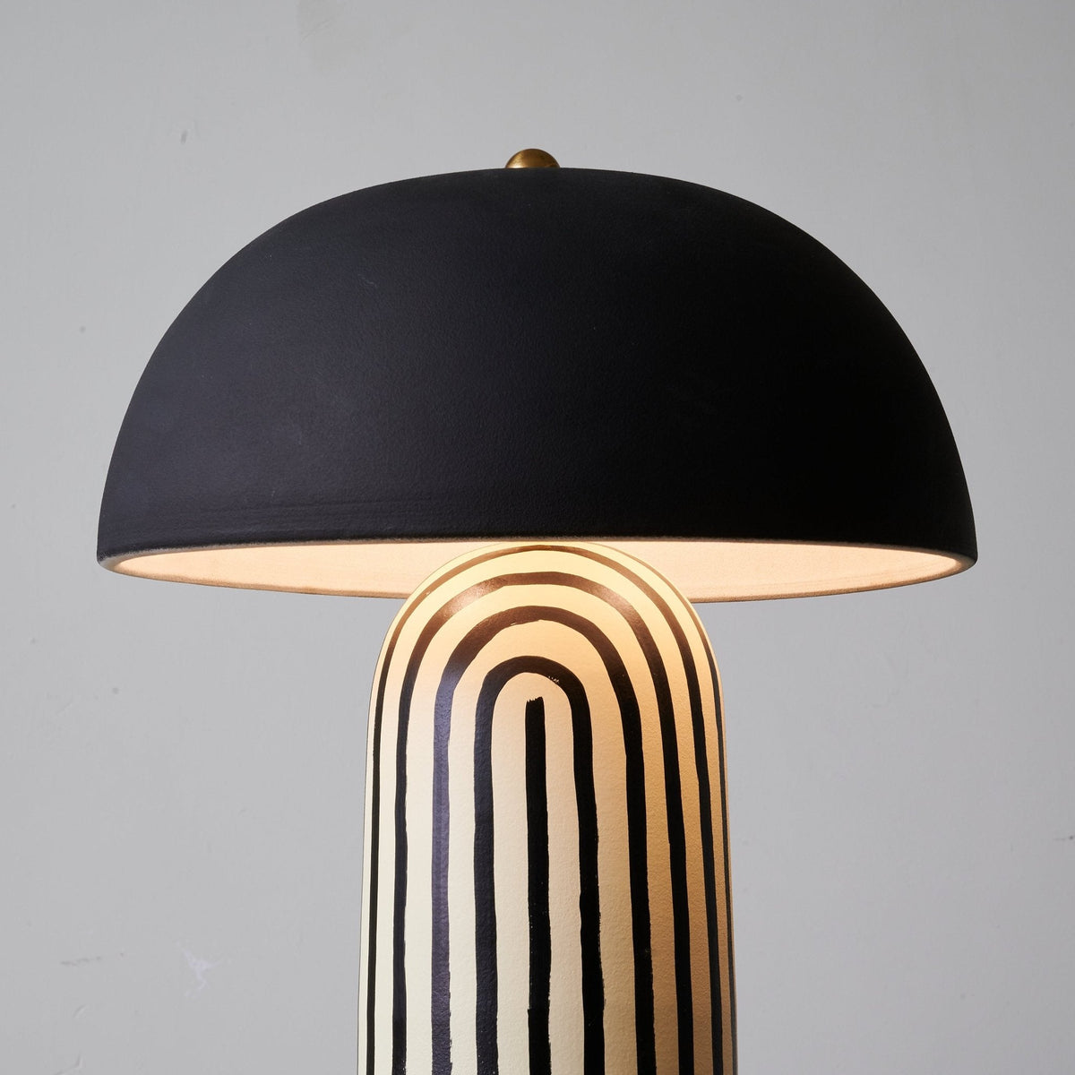 A close studio view of this Clérachic table lamp shows its matte black dome shade above the hand-painted striped ceramic base.