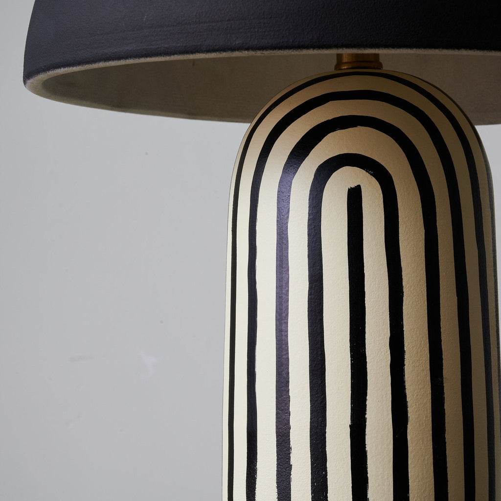 A close-up shows the arched black-and-white stripes of this Clérachic table lamp's ceramic base meeting the dome shade's rim.
