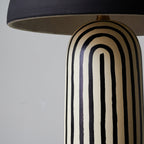 A close-up shows the arched black-and-white stripes of this Clérachic table lamp's ceramic base meeting the dome shade's rim.