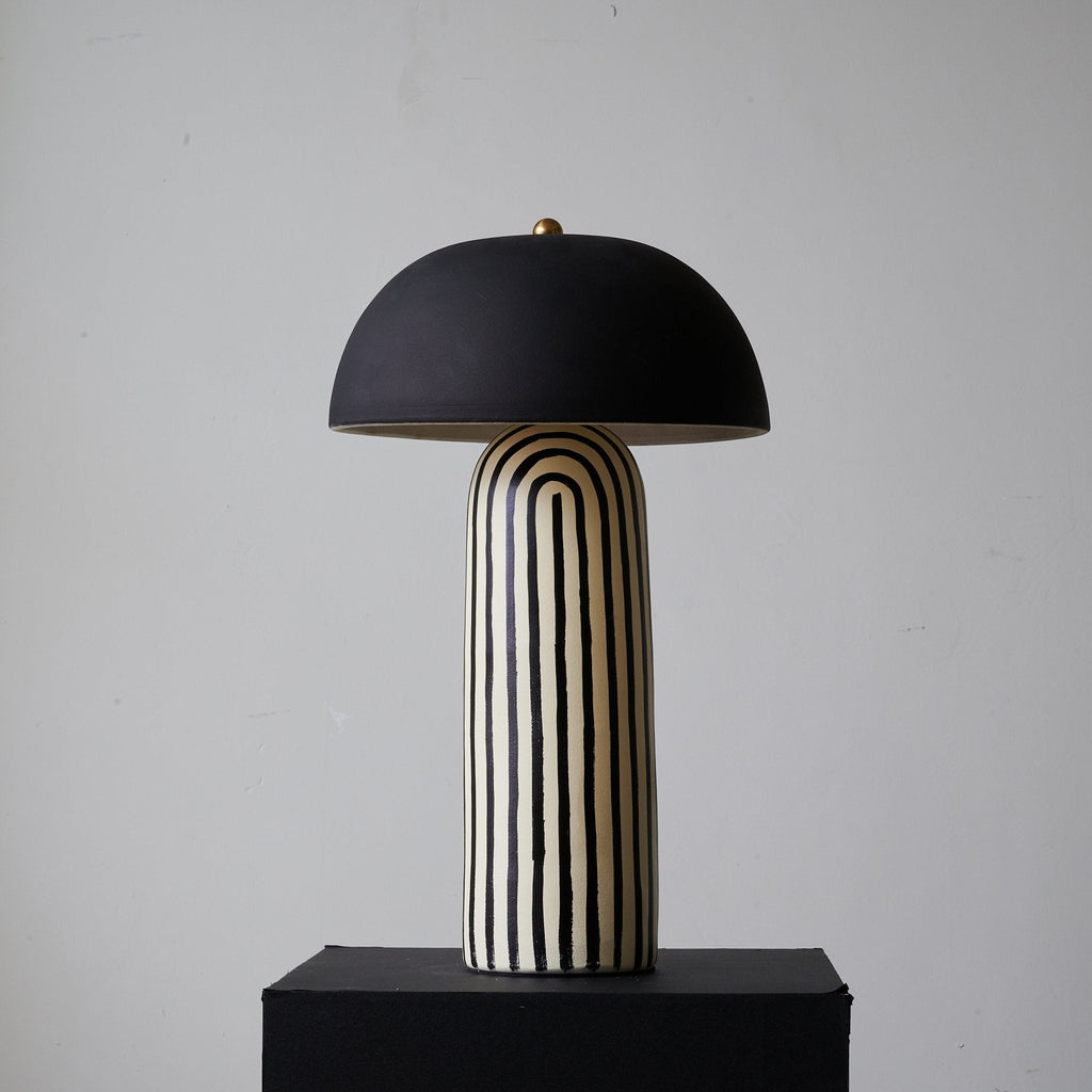 Turned to a three-quarter angle on its black plinth, this Clérachic table lamp shows the striped base beneath its dome shade.
