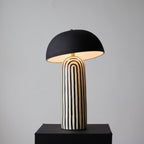 Set on a black plinth against a grey backdrop, this Clérachic table lamp shows its dome shade's pale interior above the striped base.