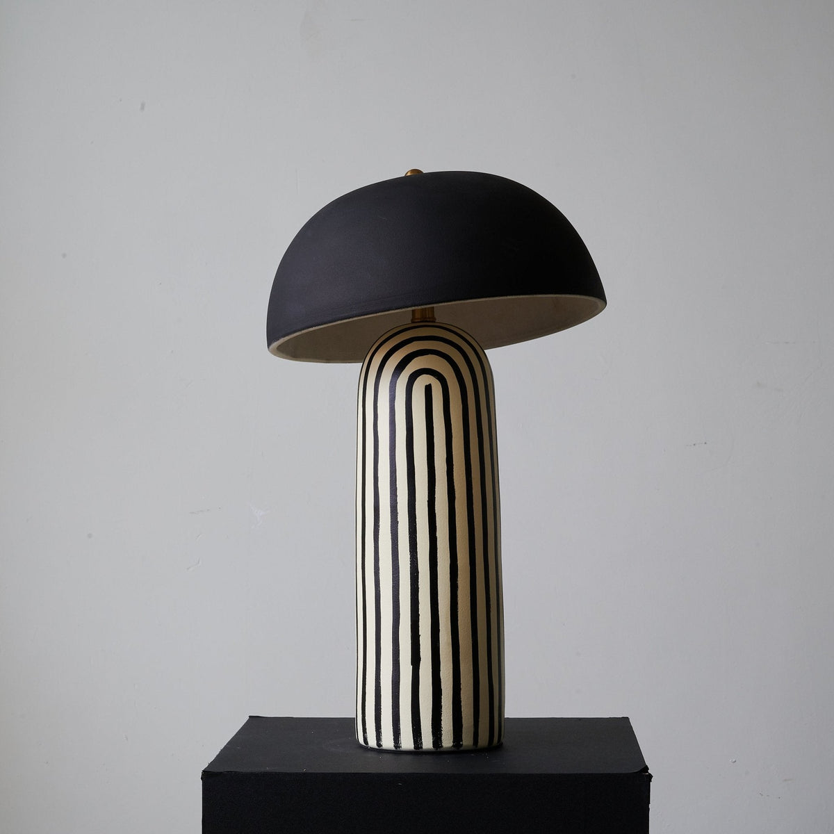 Centred on its black plinth, this Clérachic table lamp shows the dome shade above the vertically striped ceramic base.