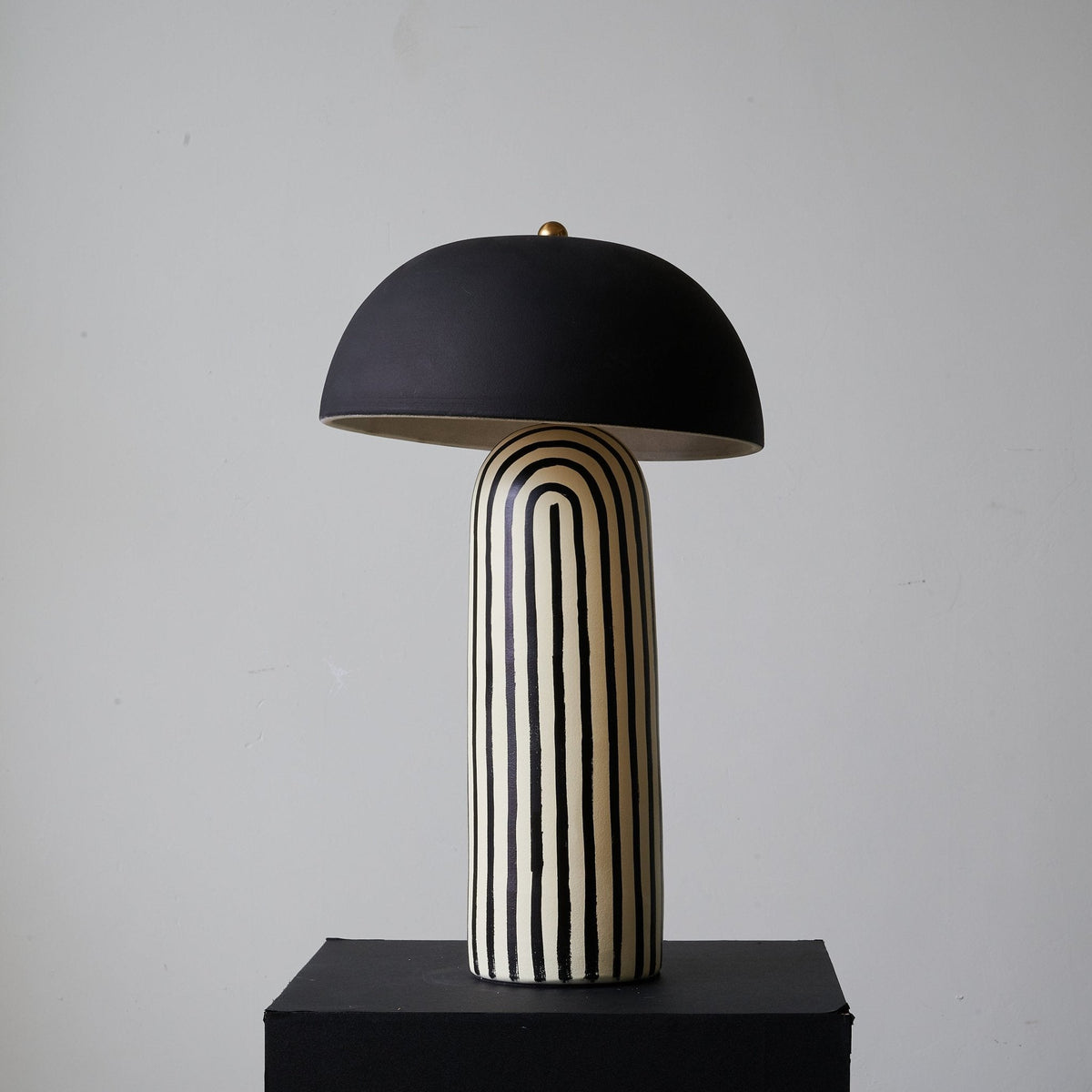 This Clérachic table lamp stands squarely on its black plinth, the ceramic base's stripes running the full height beneath the dome.