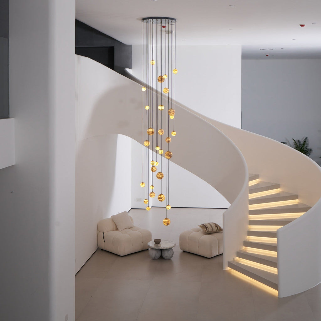 Full room in daylight: the lit Sultana chandelier beside a white spiral stair with illuminated treads.
