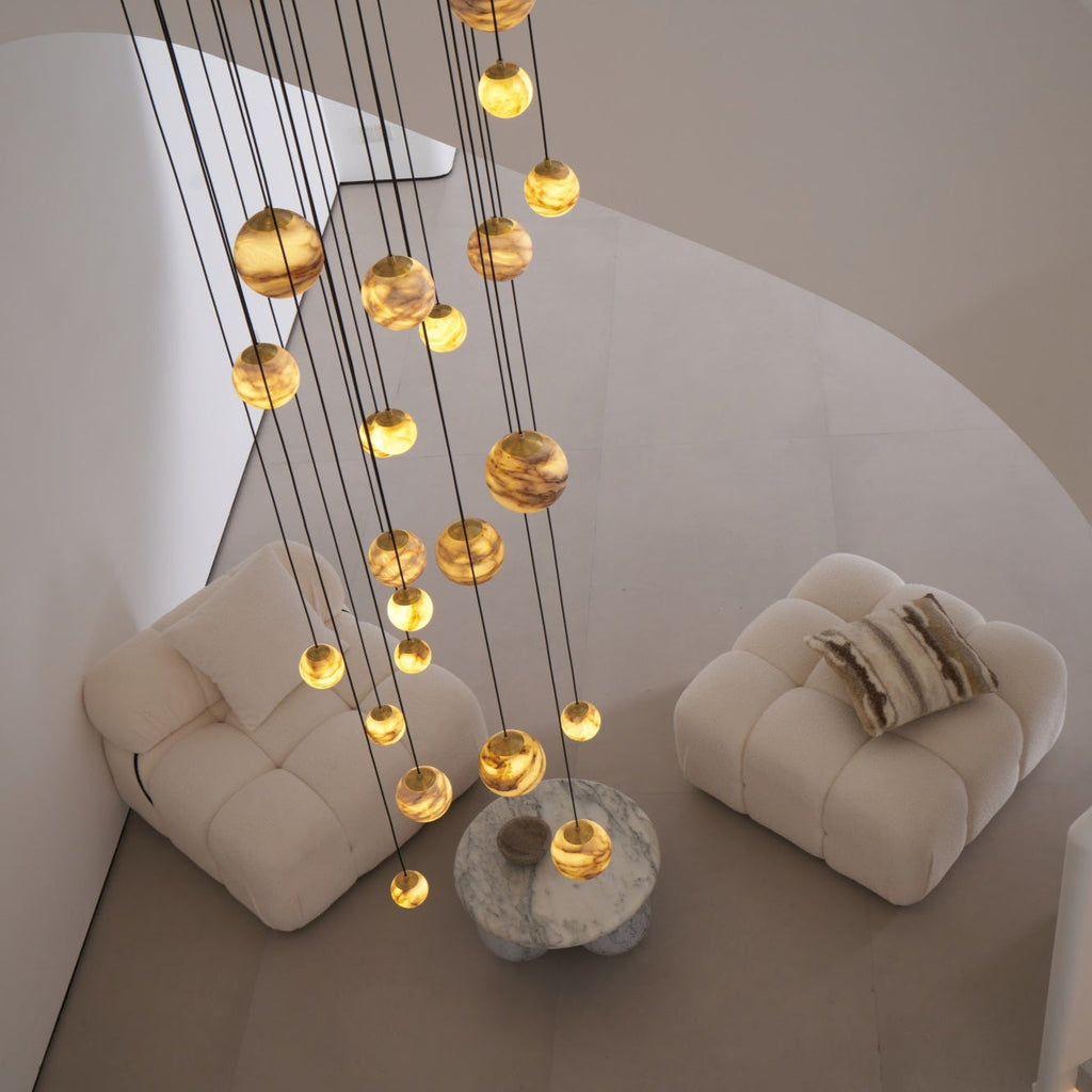 Angled overhead daylight view of the lit globes descending toward a marble table between two armchairs.