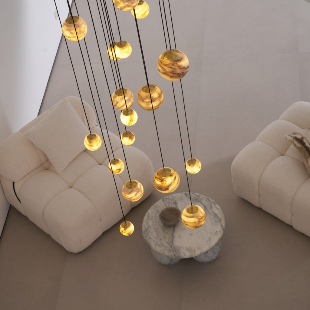 Lit alabaster globes hanging low over a round marble table set between two cream boucle armchairs.