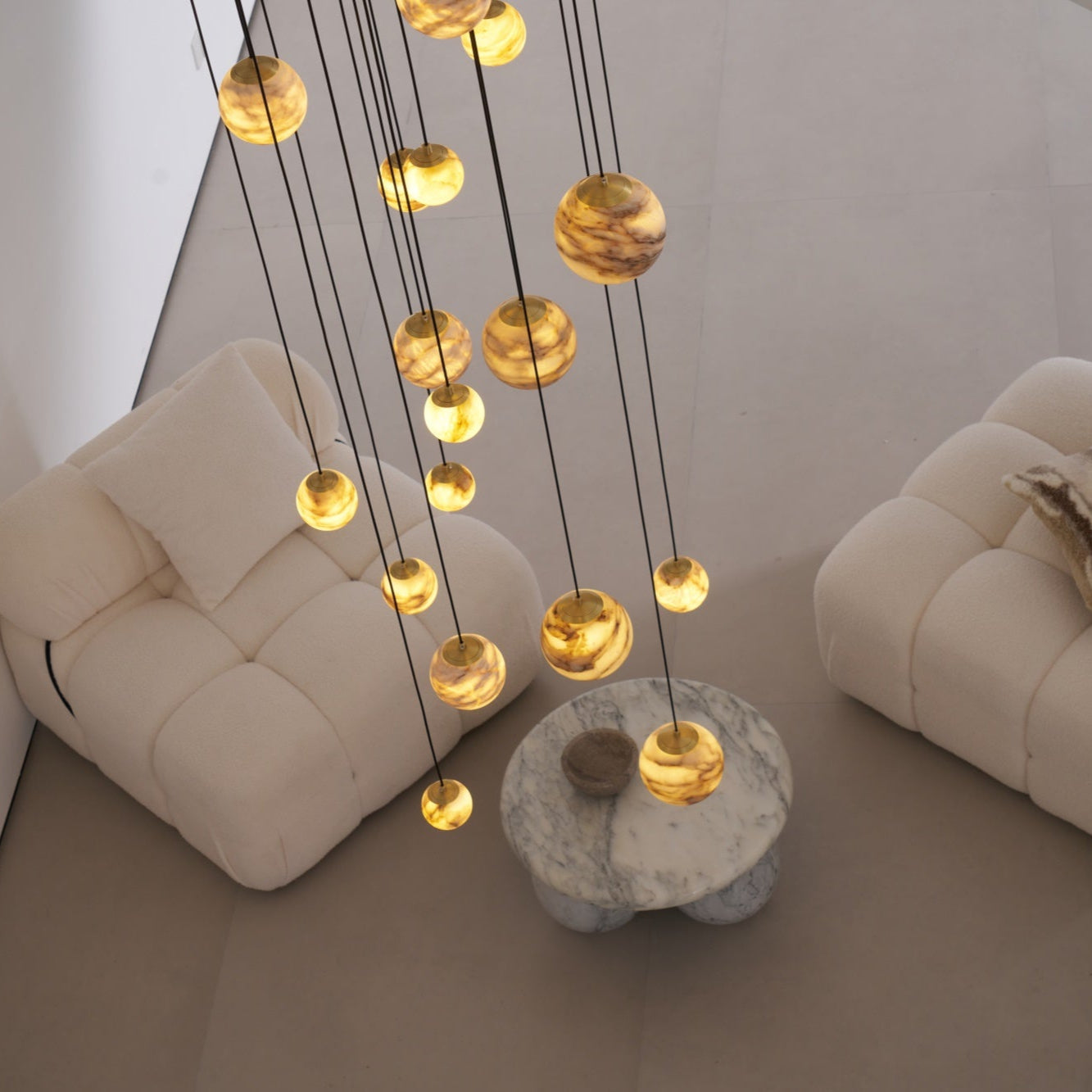 Lit alabaster globes hanging low over a round marble table set between two cream boucle armchairs.