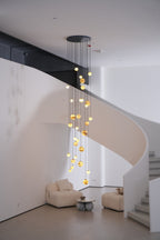 The Sultana chandelier lit in a double-height stairwell, its cascade tracing a white spiral stair.