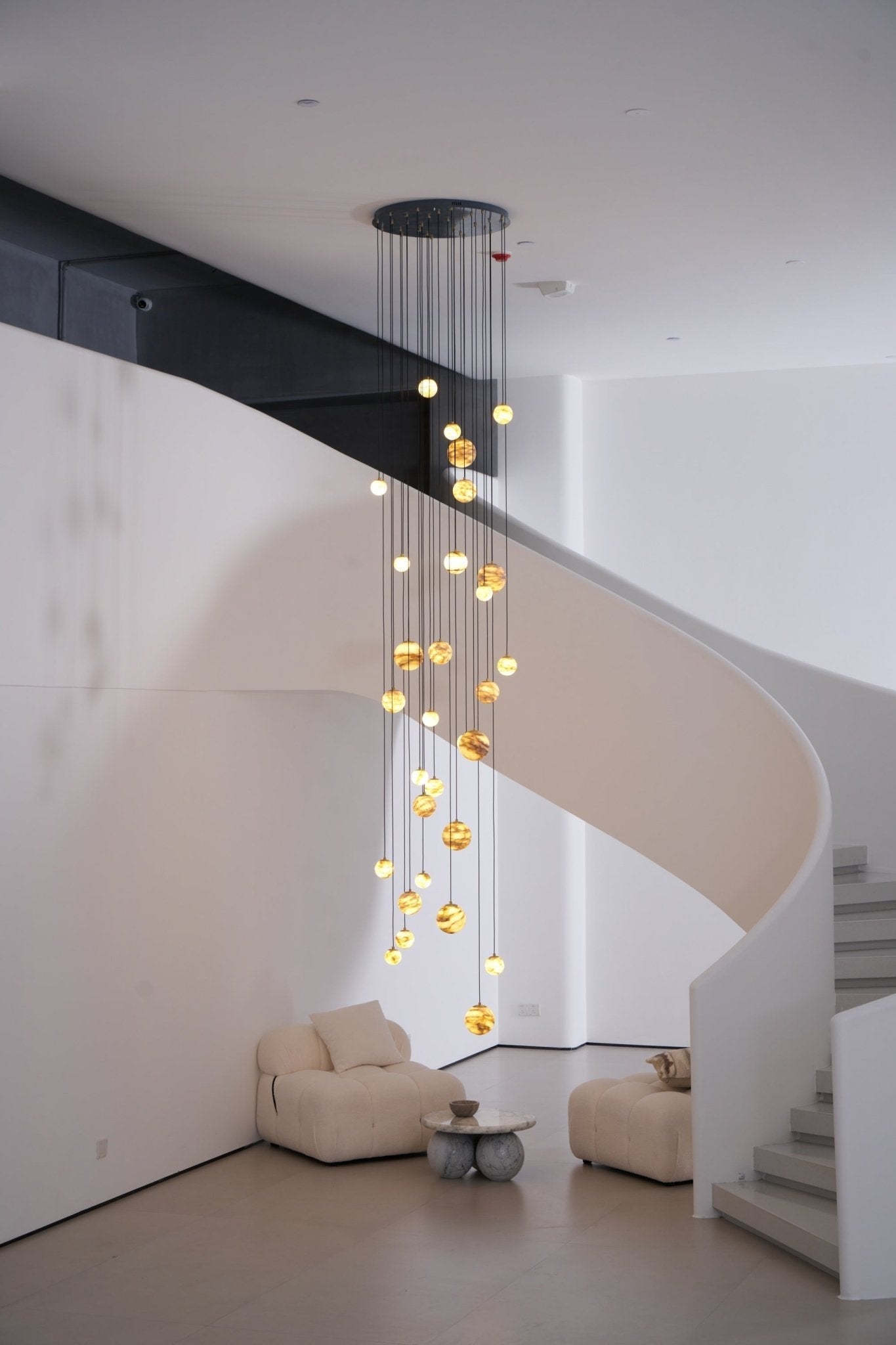 The Sultana chandelier lit in a double-height stairwell, its cascade tracing a white spiral stair.