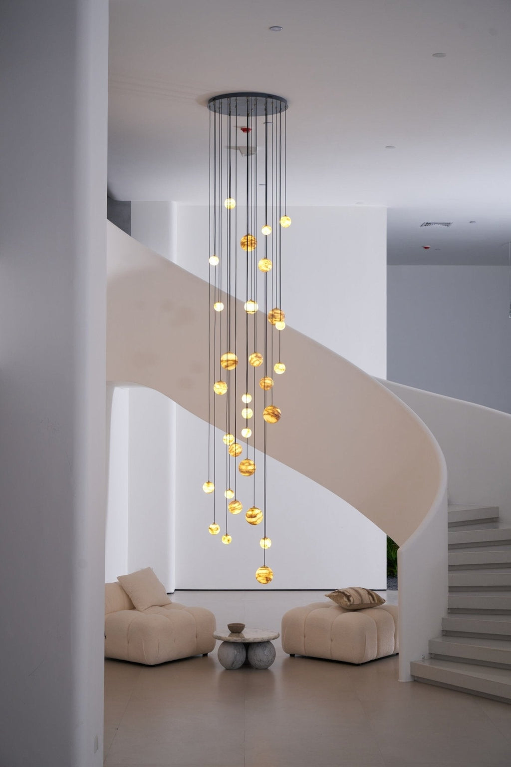 Wider daylight framing with the lit chandelier centred above two low boucle lounge chairs.