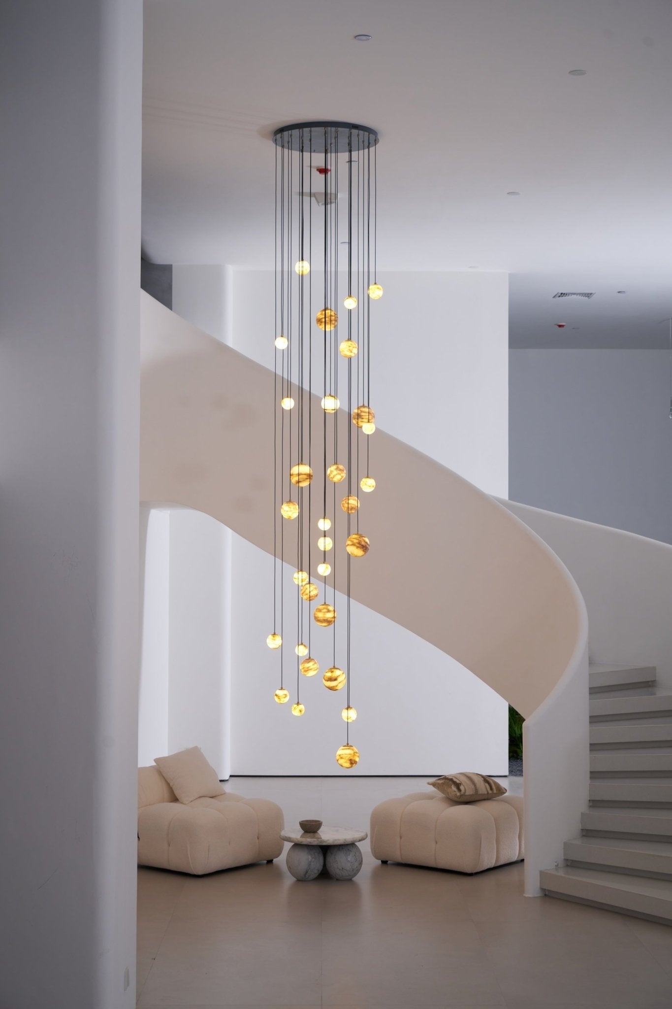 Wider daylight framing with the lit chandelier centred above two low boucle lounge chairs.