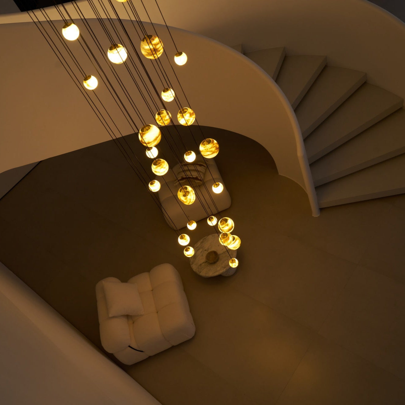 Looking down on the lit chandelier at night, the spiral stair treads curving away to the right.