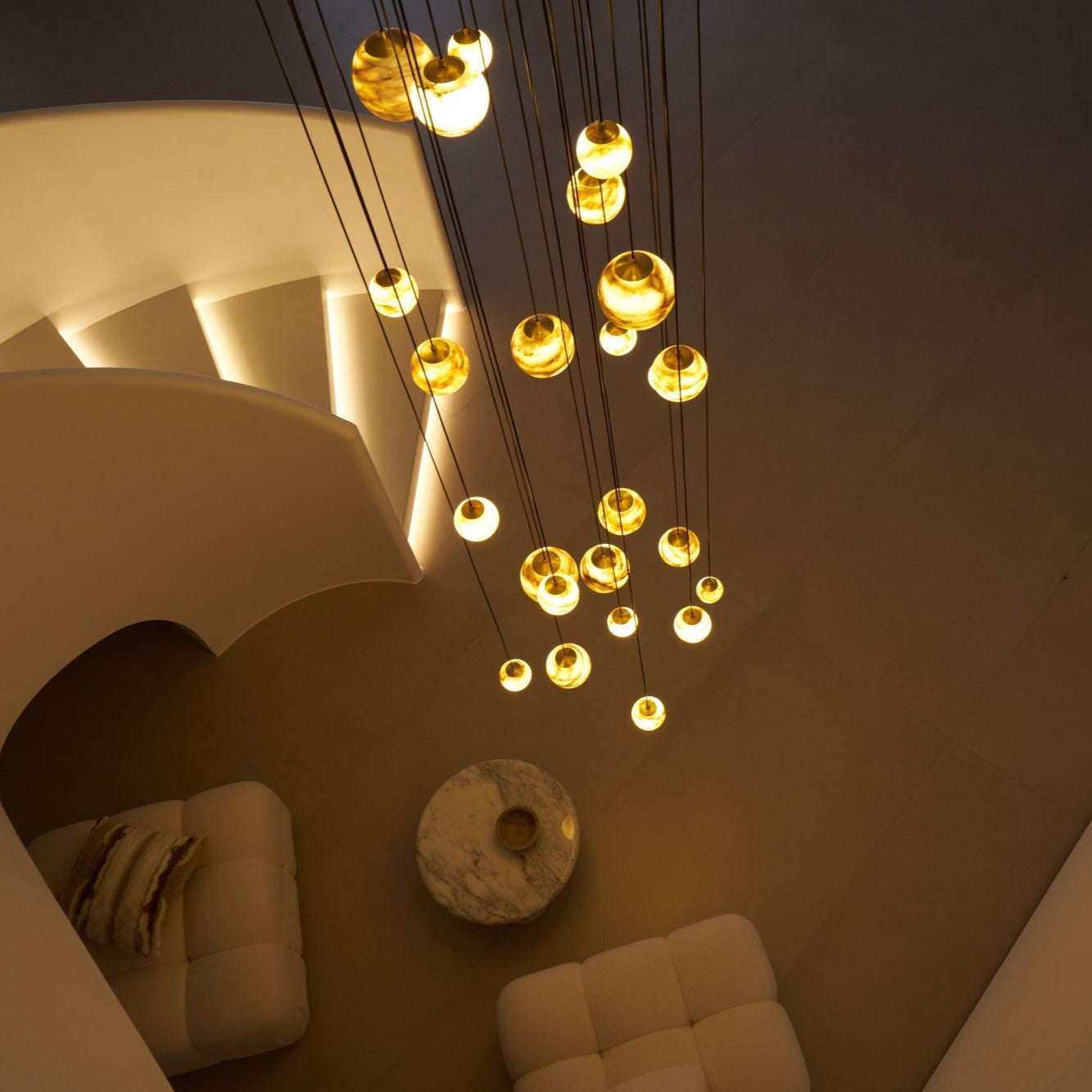 Another overhead night angle, lit globes hanging above a round marble table and two boucle seats.