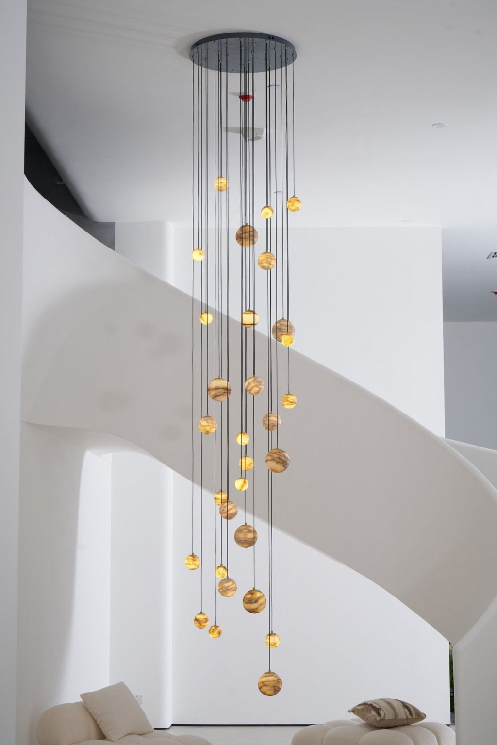 Full-height portrait view of the lit chandelier hanging beside the pale ribbon of the spiral stair.