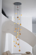 Full-height portrait view of the lit chandelier hanging beside the pale ribbon of the spiral stair.