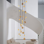Daylight view of the lit chandelier hanging clear of the staircase, globes glowing honey-gold.