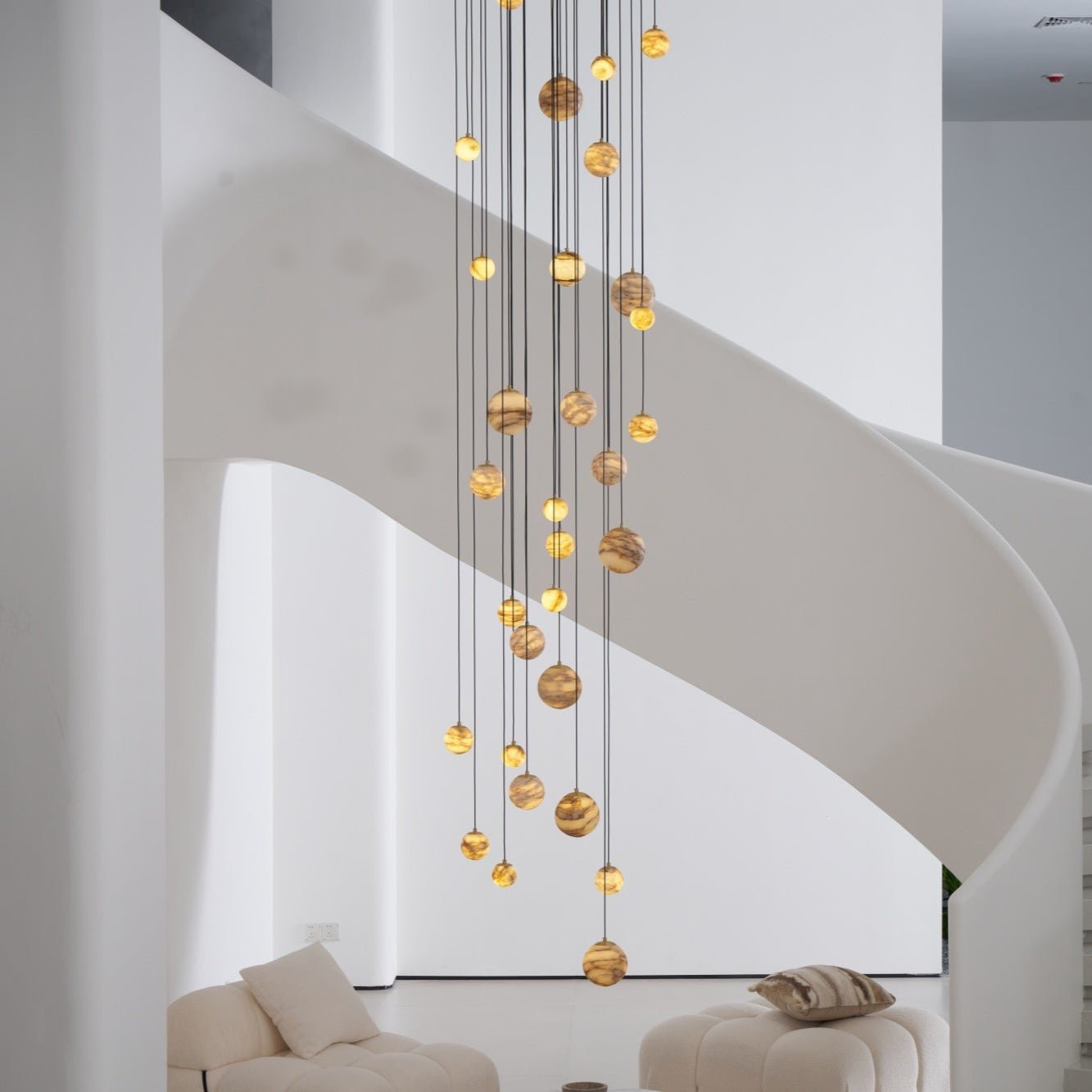 Daylight view of the lit chandelier hanging clear of the staircase, globes glowing honey-gold.