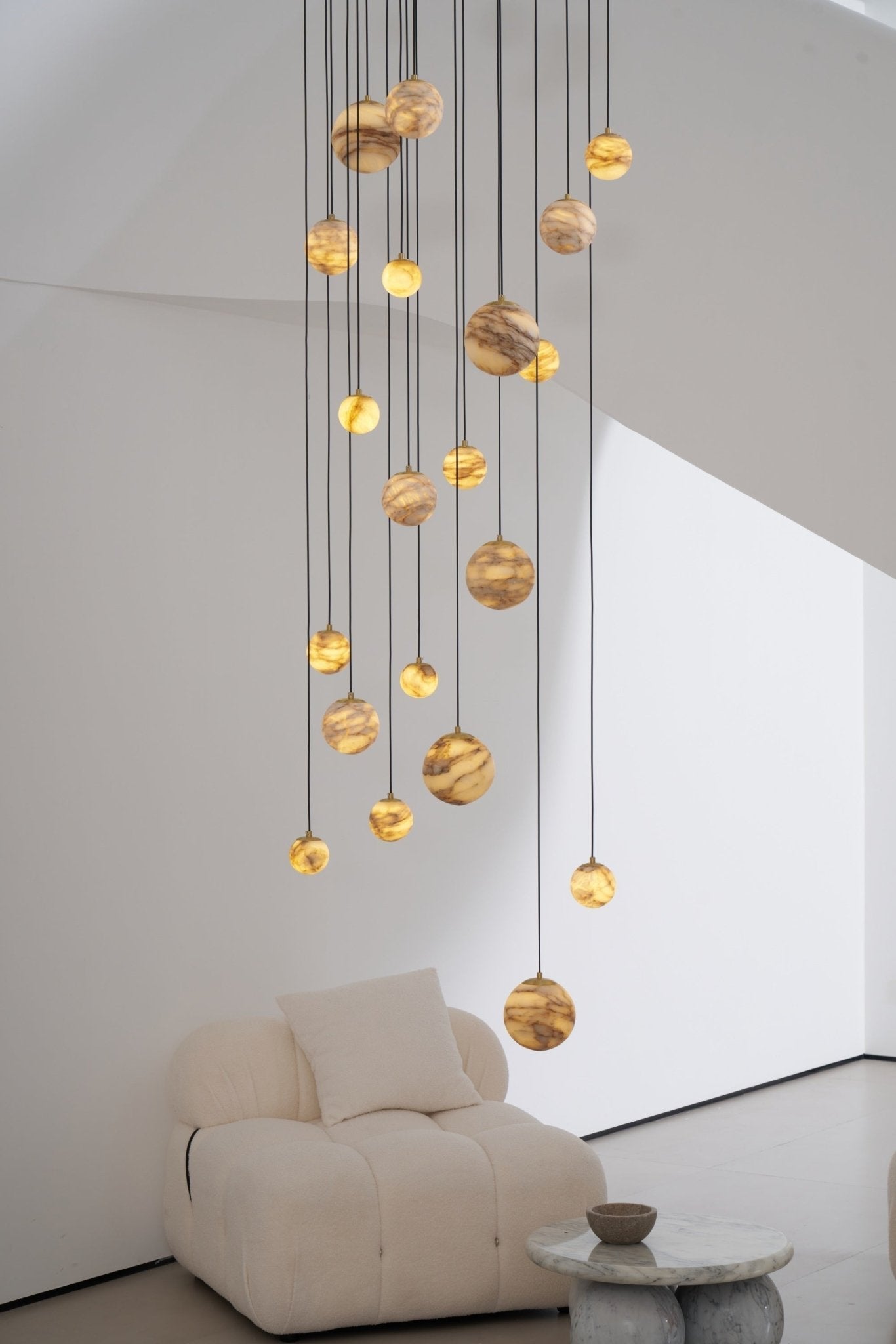 Portrait crop of the lit lower globes hanging just above a cream boucle armchair and marble table.